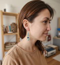 Gros plan d'un mannequin de profil portant une boucle d'oreille artisanale Artisanat Zenka composée de perles turquoises et bleu cobalt avec détails dorés, dans un décor d'atelier.