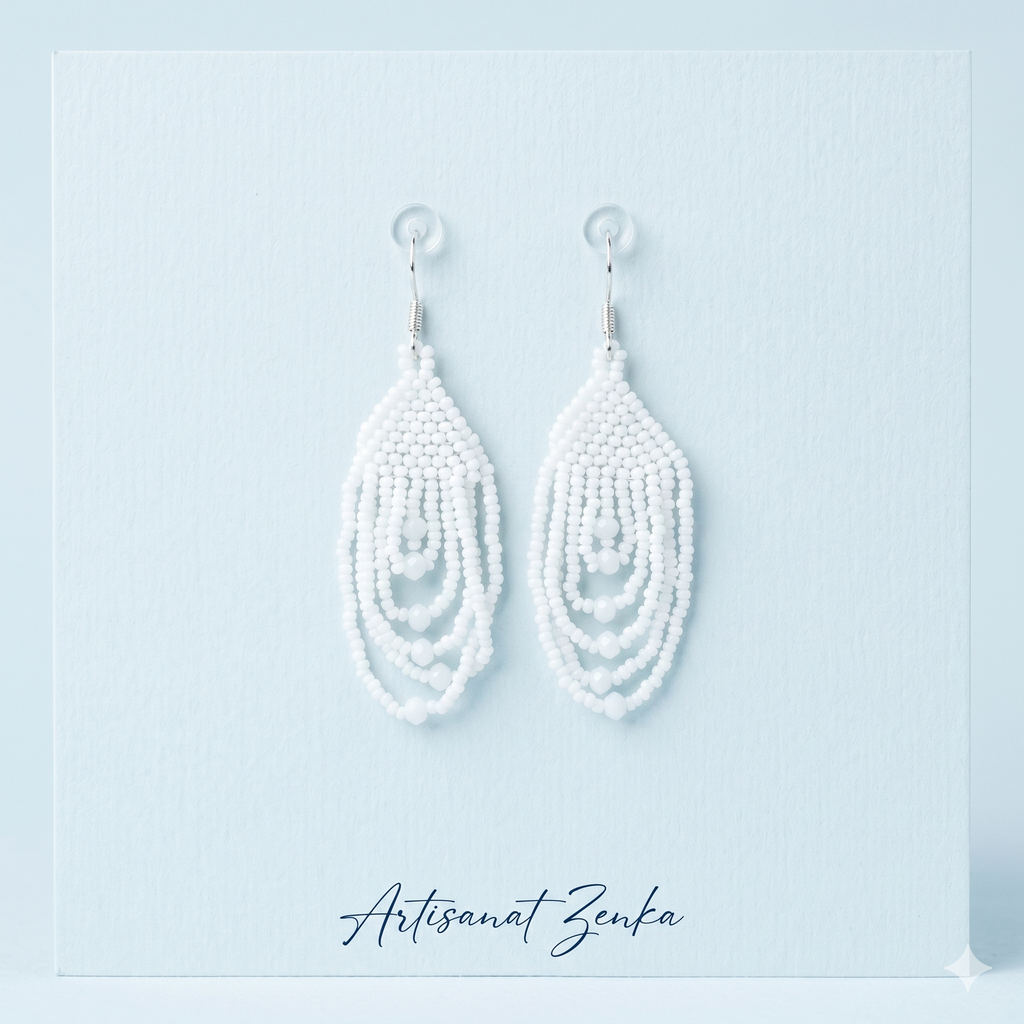 Paire de boucles d'oreilles pendantes en perles blanches de la marque Artisanat Zenka, présentées sur un support bleu pâle avec signature élégante.