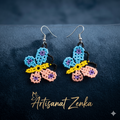Photo professionnelle des boucles d'oreilles papillon en perles bleues, jaunes et roses sur fond velours bleu marine avec logo doré Artisanat Zenka.