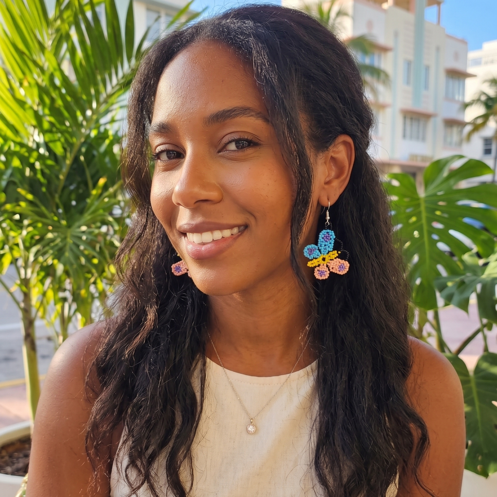 Femme souriante à Miami portant des boucles d'oreilles artisanales en perles de rocaille en forme de papillon bleu, jaune et rose.