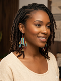 Portrait de face d'une femme portant les boucles d'oreilles colorées Artisanat Zenka, montrant la taille réelle et l'éclat des perles tissées sur un fond neutre.