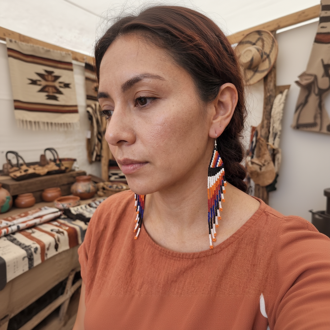 Un gros plan sur le profil d'une  belle,  portant une paire de longues boucles d'oreilles pendantes tissées en perles colorées (bleu, orange, noir, rouge) d'Artisanat Zenka, dans un marché artisanal.