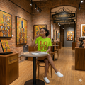 Femme assise buvant un café et portant le t-shirt vert lime LOVE avec imprimé géométrique Kente, décor Galerie Ateliers BECCAR.