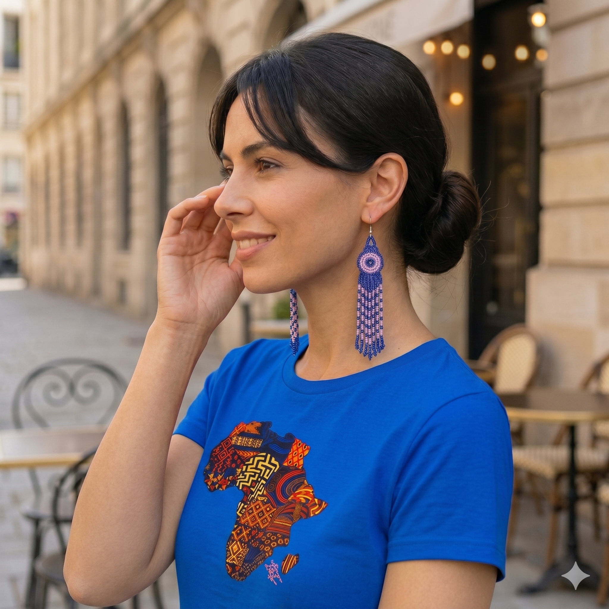 Femme portant un t-shirt bleu avec motif carte d'Afrique multicolore et boucles d'oreilles artisanales.