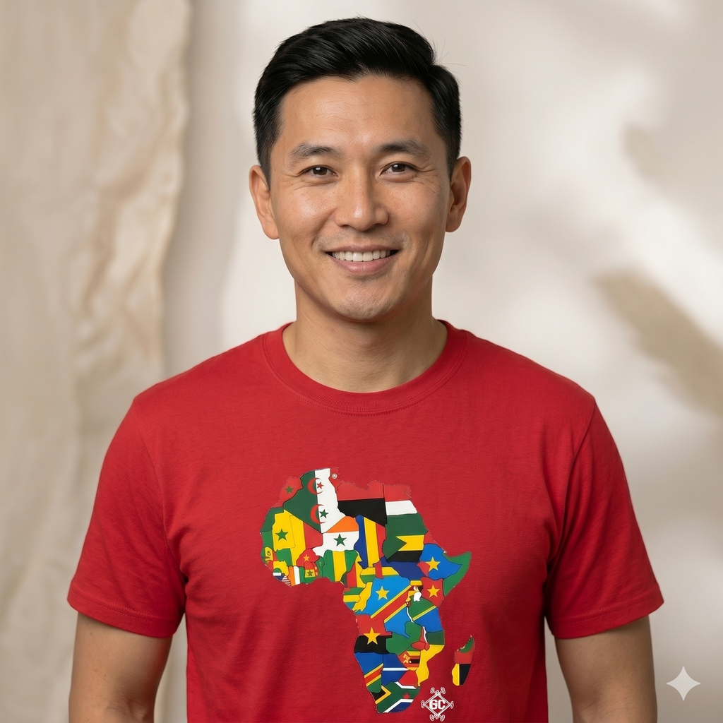 Photo de face d'un homme  souriant, portant un t-shirt rouge à manches courtes. Le t-shirt présente un motif central de la carte du continent africain remplie par une mosaïque des drapeaux de tous les pays africains. Arrière-plan de studio doux.