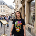 Femme portant un t-shirt noir unisexe avec un motif de crâne mexicain coloré et fleurs dans les rues historiques de Luxembourg.