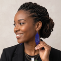 Femme  élégante en blazer noir touchant une boucle d'oreille bleue en perles pour la mettre en valeur, profil souriant.