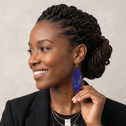 Femme  élégante en blazer noir touchant une boucle d'oreille bleue en perles pour la mettre en valeur, profil souriant.