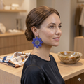 Gros plan de profil d'une femme souriante portant les boucles d'oreilles fleurs en perles bleues, mettant en valeur l'éclat du bijou.