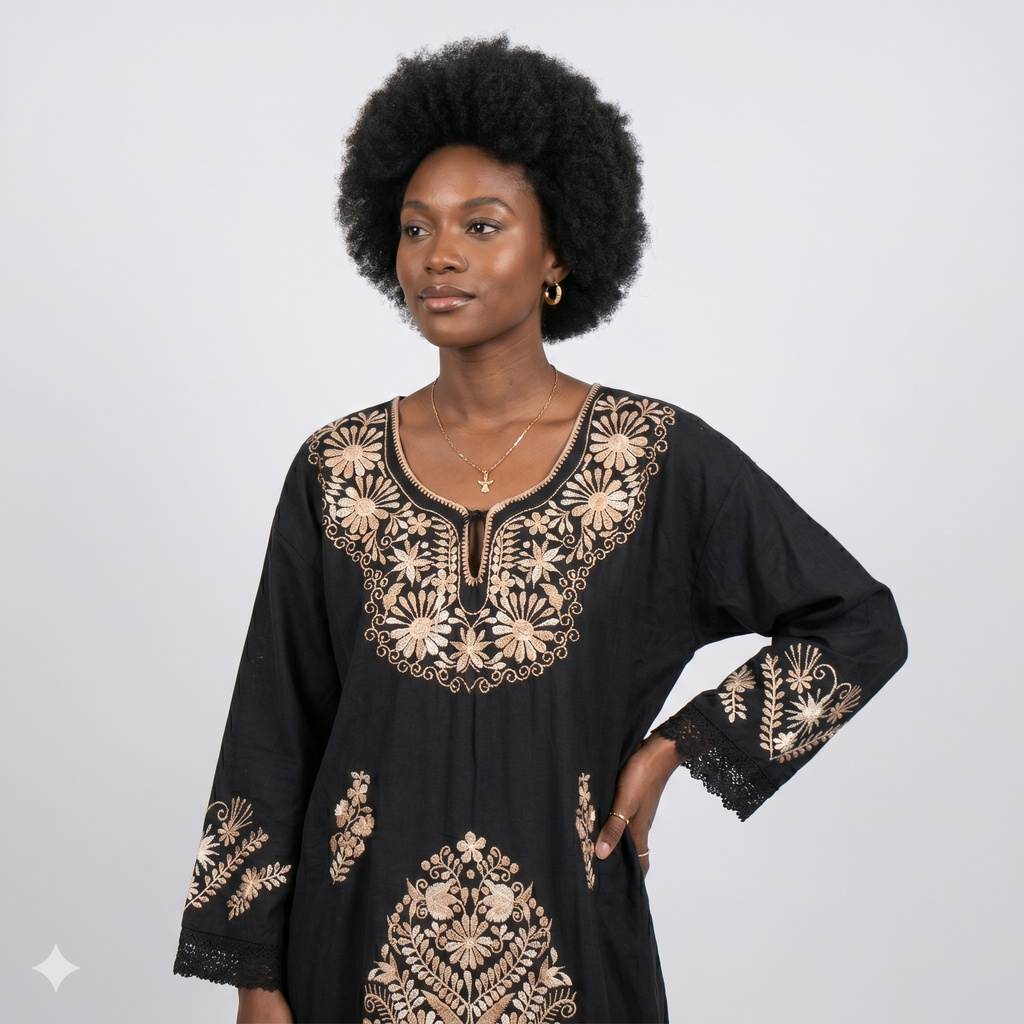 Femme noire avec une coiffure afro portant la robe caftan noire, soulignant le contraste entre les broderies dorées et le noir profond, ainsi que les détails en dentelle aux poignets.