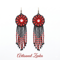 Paire de boucles d'oreilles artisanales Artisanat Zenka en perles rouges, noires et blanches avec médaillon central et longues franges perlées sur fond blanc.