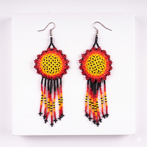 Paire de boucles d'oreilles artisanales de style amérindien avec motif solaire central et franges perlées rouges, jaunes et noires sur fond blanc.